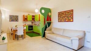 A modern kitchen with green cabinets, a dining area with a white table and chairs, and a beige sofa in a living room. - Welc-om Green Cottage (Teolo)