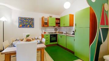 A kitchen with green cabinets, a dining table with chairs, and a colorful abstract painting on the wall.