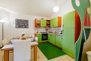 A kitchen with green cabinets, a dining table with chairs, and a colorful abstract painting on the wall. - Welc-om Green Cottage (Teolo)