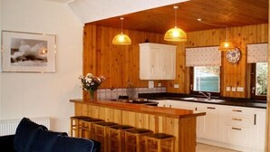 Une cuisine chaleureuse aux murs en bois, dotée d’un îlot central avec des tabourets de bar et d’un éclairage suspendu.