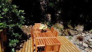 Une terrasse en bois avec une table et des chaises, entourée de verdure et de rochers.
