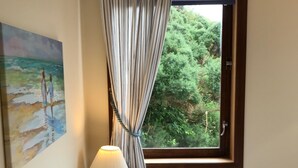 Une chambre d’hôtel avec un lit, une table de chevet avec une lampe, un tableau représentant une scène de plage et une fenêtre avec des rideaux.