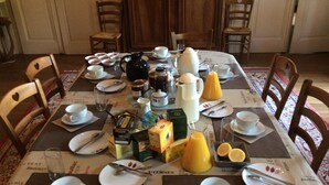 A dining table set with white plates, cups, and cutlery, surrounded by wooden chairs. - Manoir de Curty (Imphy)