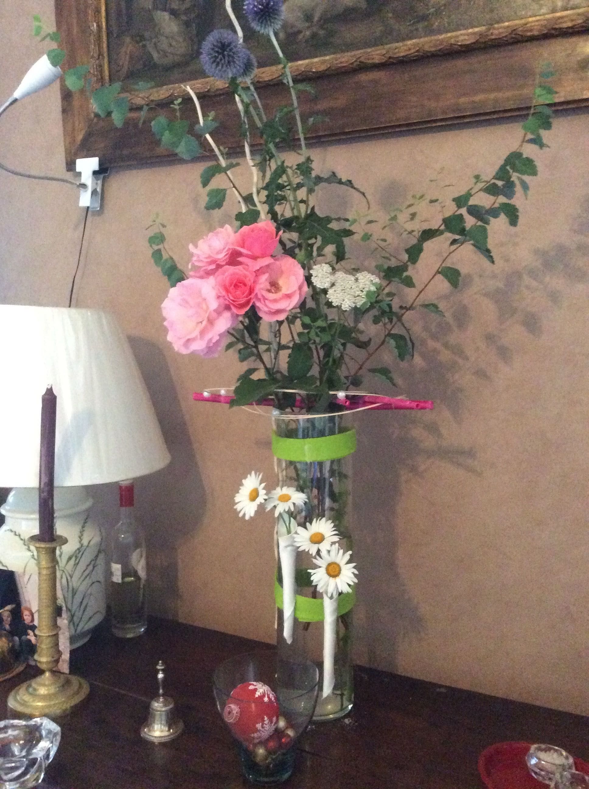 Een vaas met roze rozen en witte margrieten op een tafel, een kaars en een lamp.