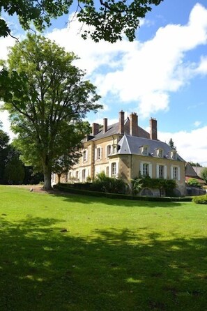 A large, historic building with multiple chimneys, surrounded by a well-maintained lawn and a large tree. - Manoir de Curty (Imphy)