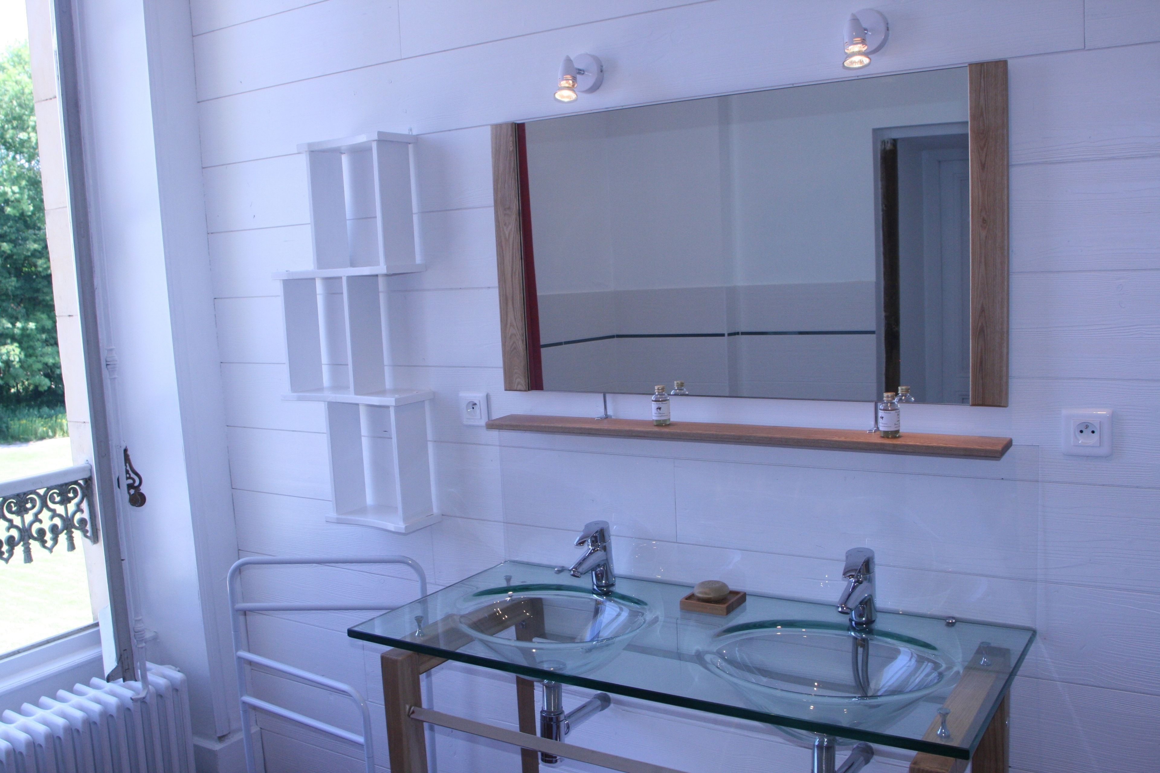 A bathroom with two glass sinks, a wooden shelf above the sinks, and a mirror with a wooden frame.