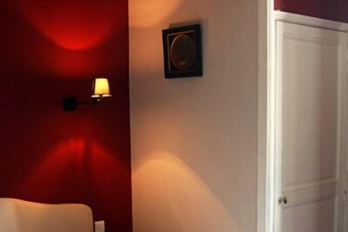 Une chambre à coucher avec un lit, une table de chevet, une lampe fixée au mur et une porte.
