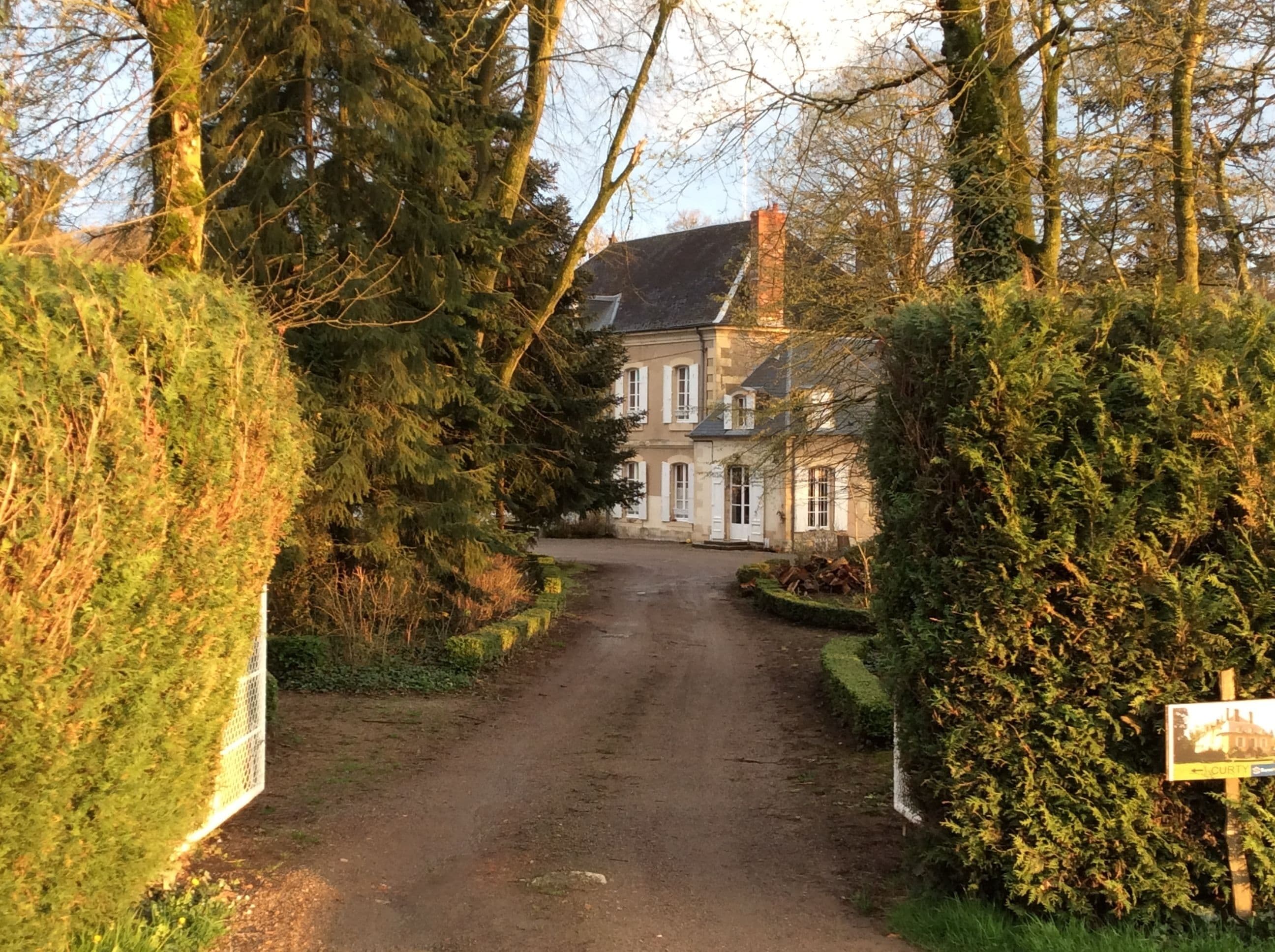 A rural road leading to a stone building with a traditional design, surrounded by dense greenery and trees.