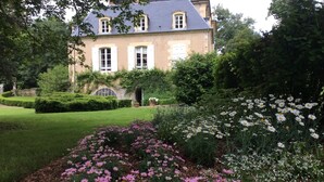 A large, historic house with a well-maintained garden featuring pink and white flowers, a manicured lawn, and a stone wall. - Manoir de Curty (Imphy)