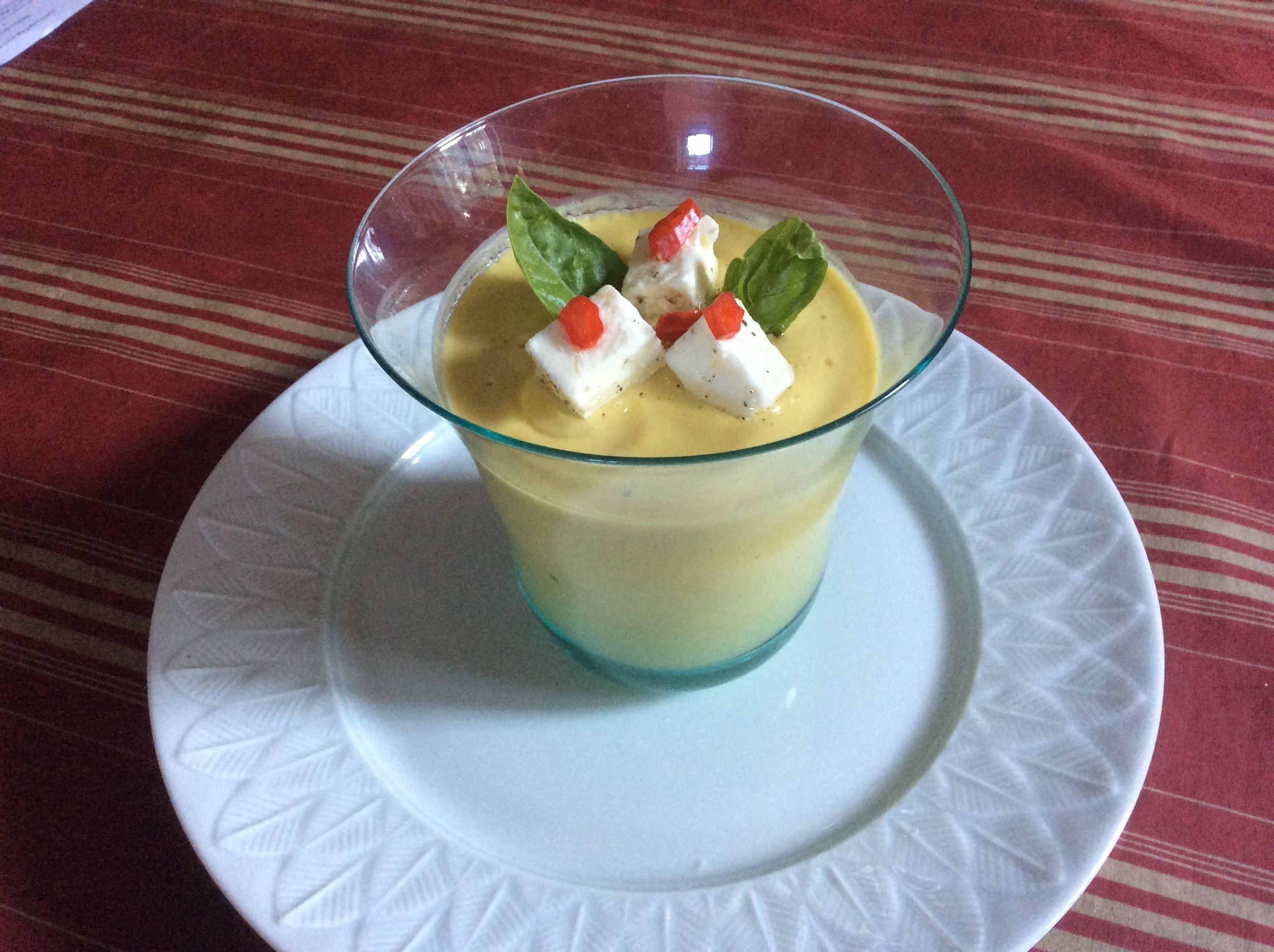 Un dessert servi dans un verre, posé sur une assiette blanche, le tout sur une nappe rouge.