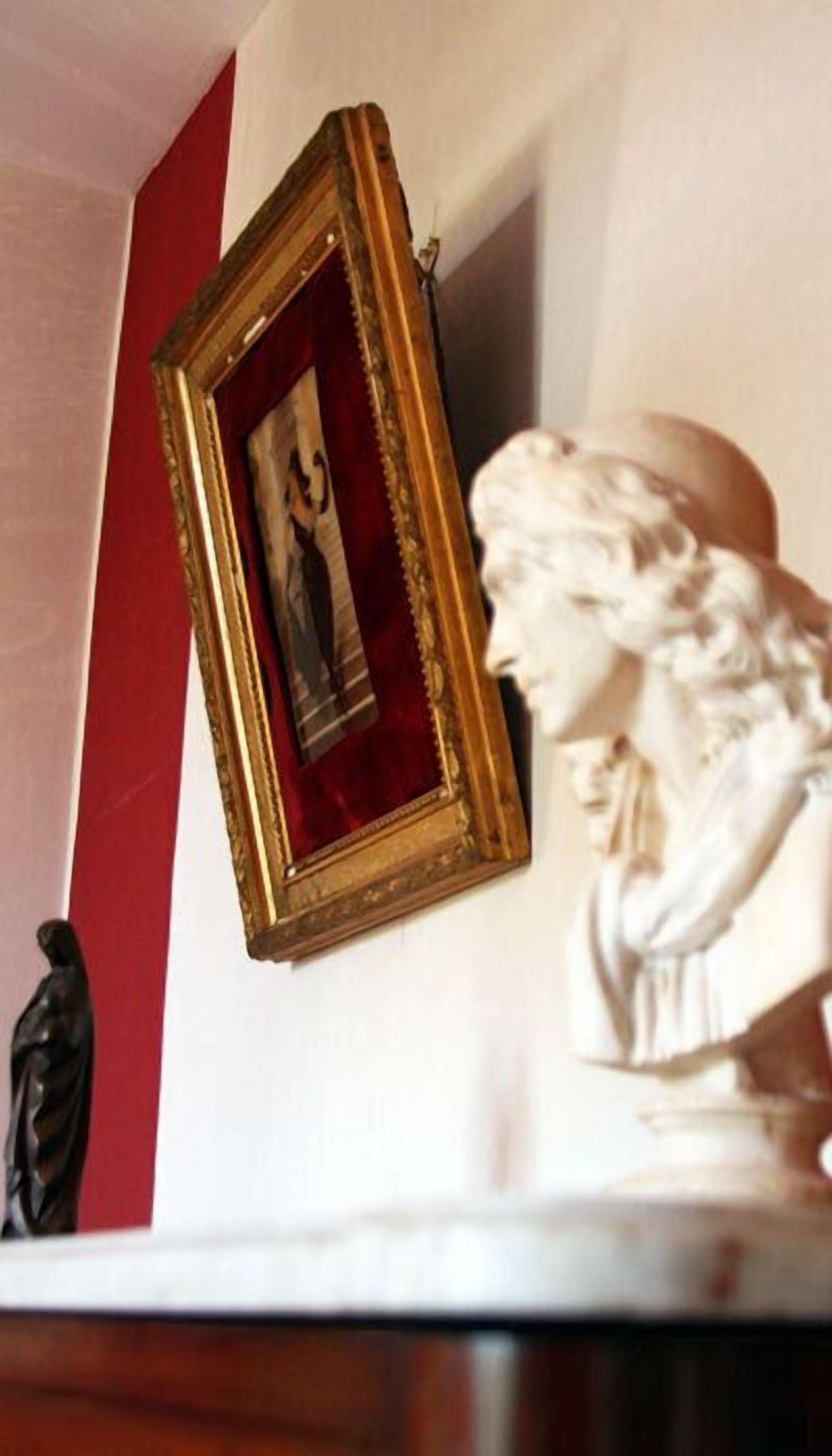 A framed picture on a wall with a statue beside it.