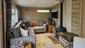 Ein gemütliches Wohnzimmer mit einer Couch, einem Couchtisch, einem Kamin und einem an der Wand befestigten Fernseher.