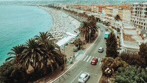 A coastal cityscape with a beach, palm trees, and a road with cars. - Appartment sympa 4p, près des musées et de la gare (Nice)