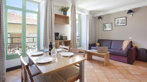 A dining area with a table set for two, a laptop on a side table, and a sofa in the background. - Appartment sympa 4p, près des musées et de la gare (Nice)