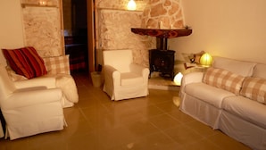 A cozy living room with a stone wall, a fireplace, and white furniture. - Beautiful Character Villa and Trullo in Ostuni Olive Grove with Private Pool (Ostuni 72017 (BR))