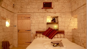 A cozy room with a wooden door, a bed with a heart-shaped pillow, a small shelf with decorative items, and a wall-mounted light. - Beautiful Character Villa and Trullo in Ostuni Olive Grove with Private Pool (Ostuni 72017 (BR))
