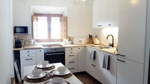 Moderni keittiö, jossa on valkoiset kaapit, sisäänrakennettu uuni, mikroaaltouuni ja pesuallas. Työtasolla on neljä kulhoa, ja vedenkeitin on näkyvillä.
