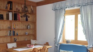 Een knus ingerichte kamer met een houten eettafel, stoelen, een blauwe bank en een boekenkast vol boeken en decoratieve objecten.