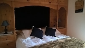 Een bed met een donker hoofdbord, wit beddengoed en twee donkere kussens. Aan weerszijden van het bed staan houten nachtkastjes met lampen.