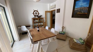 A dining area with a wooden table, white chairs, a ship's wheel decoration, a bookshelf, and a framed picture on the wall. - Beach villa with sea view roof terrace for the whole family (Alvor)