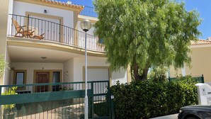 A two-story building with a balcony, a green gate, and a tree in front. - Beach villa with sea view roof terrace for the whole family (Alvor)