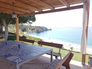 A covered outdoor seating area with a view of the beach and sea.