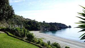 Eine Küstenlandschaft mit einer Wiese, einem gewundenen Strand und felsigen Klippen.