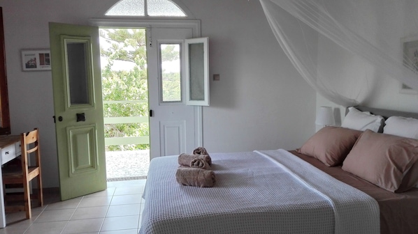 A bedroom with a bed, pillows, a green door, and a view through the door.