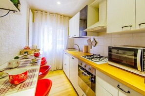 A compact kitchen with white cabinets, a gas stove, a microwave, and a dining area with a table set for four. - Welc-om Vittoria (Padova)
