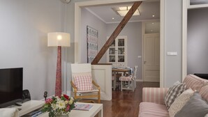 A living room with a TV, a lamp, a chair, a sofa, and a dining area with a table and chairs.