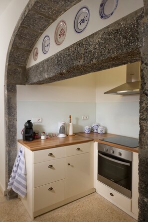 Una cocina con arco de piedra, armarios blancos, encimera de madera, horno empotrado y platos decorativos en la pared.