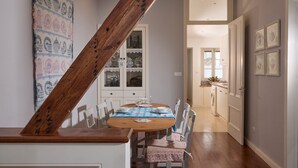 A dining area with a wooden staircase, a table set for four, and a view into the kitchen.