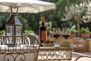 Uma mesa com uma garrafa de vinho Chianti Classico, dois copos de vinho tinto, uma tigela de uvas e um candeeiro.
