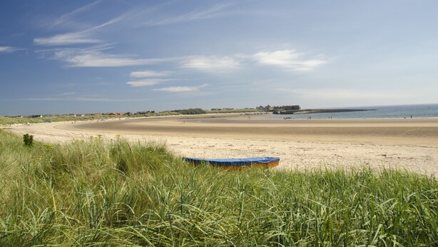 A beach with a boat in the foreground and a clear sky.