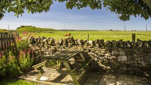 A stone wall with a wooden picnic table in a grassy field.