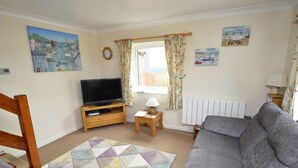 A living room with a sofa, a television on a wooden stand, a patterned rug, and a window with curtains.