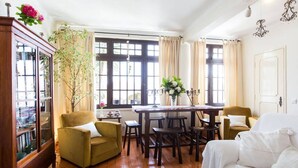 Een woonkamer met een bank, fauteuil, eettafel en stoelen. Er is een boekenkast en een plant in pot.