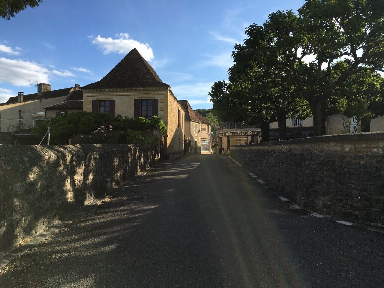 A narrow street flanked by stone walls and buildings with a bar and restaurant sign.