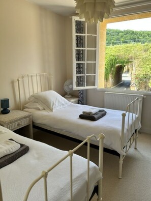 Une chambre avec deux lits, une fenêtre donnant sur un espace verdoyant et un radiateur.