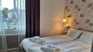A neatly made bed with white linens and towels, a bedside lamp, and a floral wallpaper. - Smålandsstenar hotell (Smalandsstenar)
