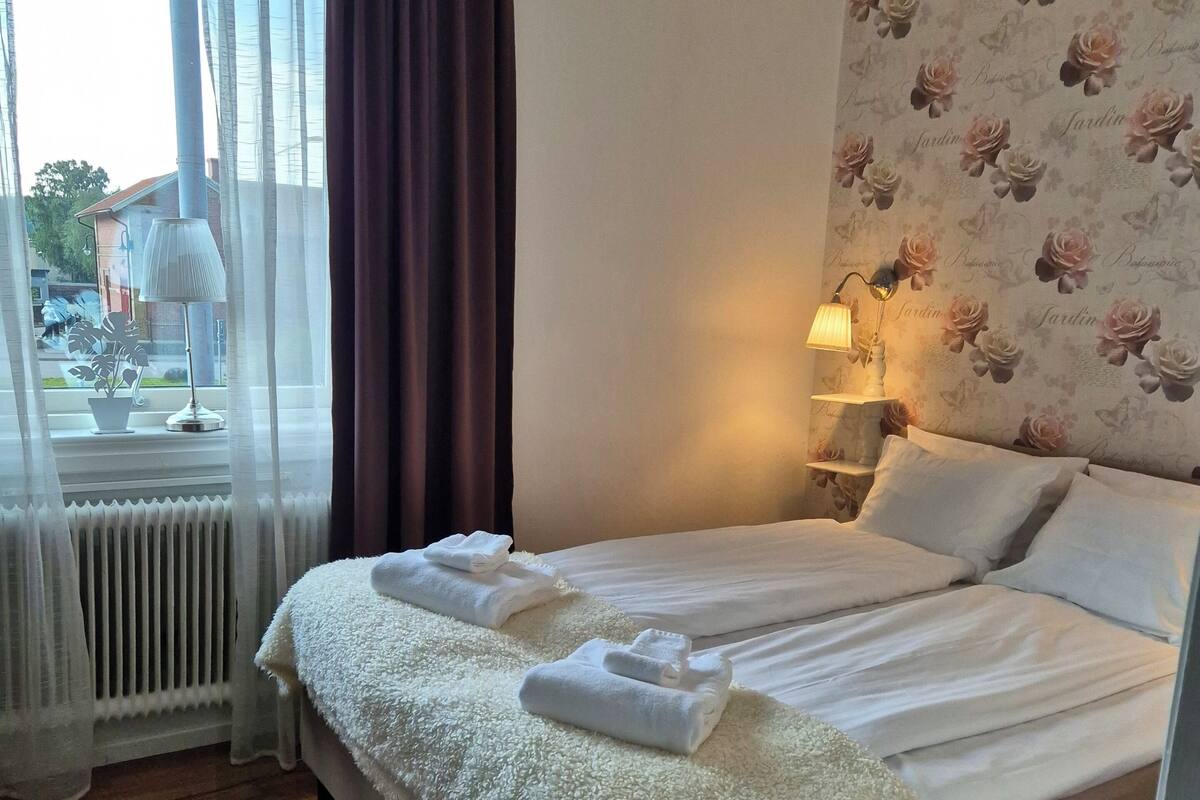 A neatly made bed with white linens and towels, a bedside lamp, and a floral wallpaper.