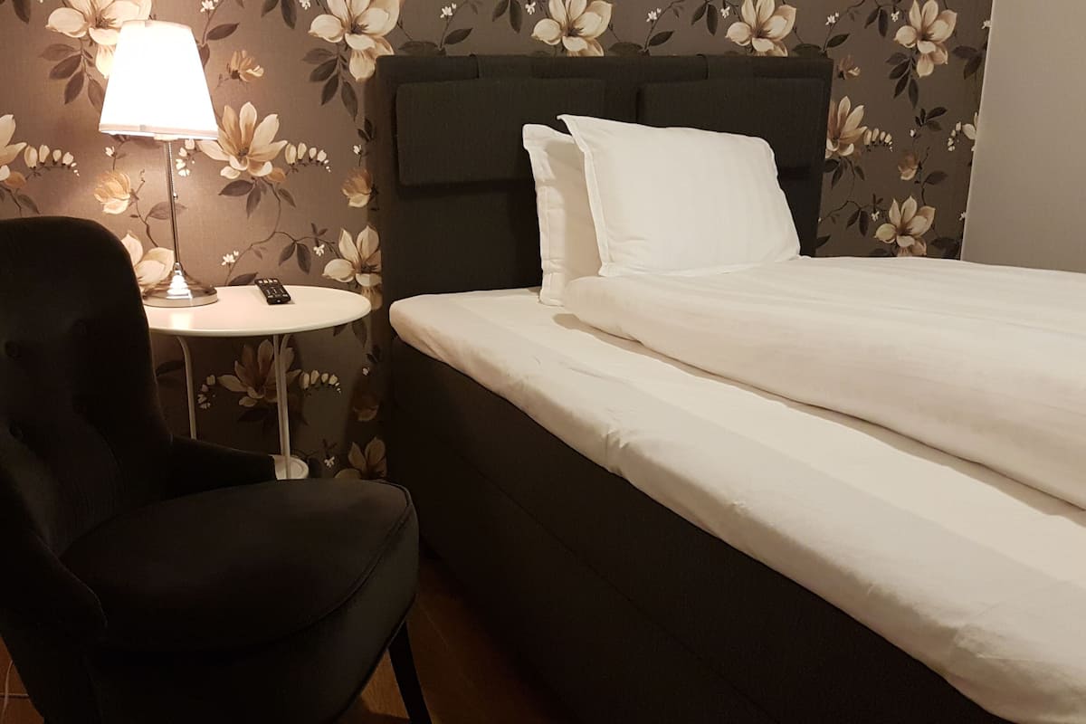 A hotel room with a bed, a chair, a small table, and a lamp.