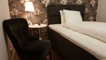 Et hotelværelse med en seng, en stol, et lille bord og en lampe.