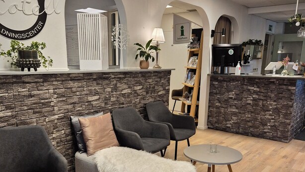 A modern reception area with a stone accent wall, a reception desk, and seating arrangements including a sofa and armchairs. - Smålandsstenar hotell (Smalandsstenar)