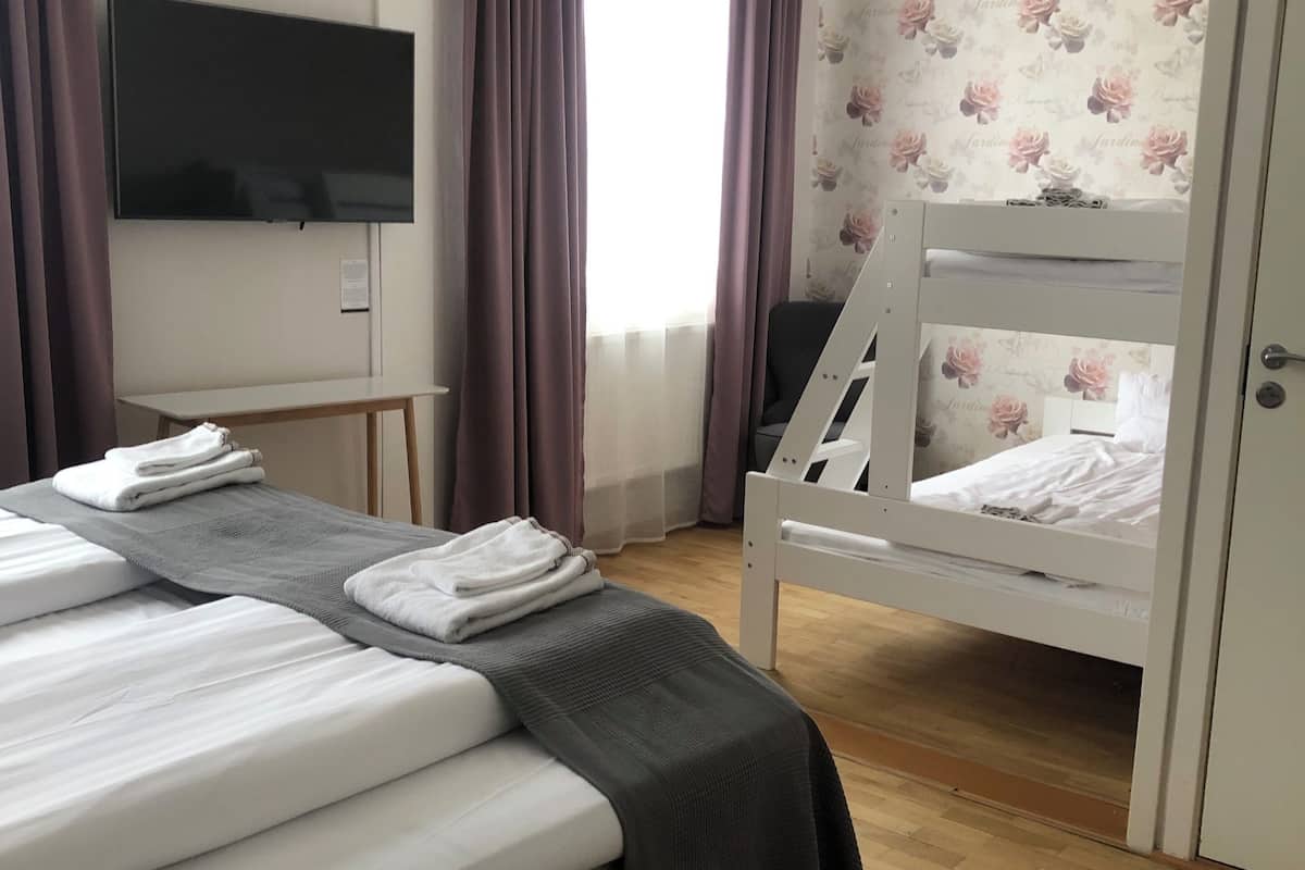 A hotel room with a large bed, a smaller bed on a bunk, a TV mounted on the wall, and a window with curtains.
