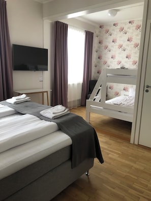 A hotel room with a large bed, a smaller bed on a bunk, a TV mounted on the wall, and a window with curtains. - Smålandsstenar hotell (Smalandsstenar)