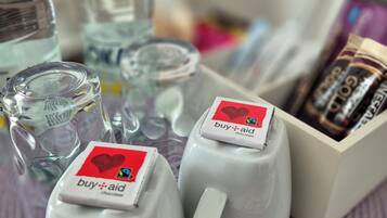 Dos tazas blancas con etiquetas que dicen 'buy-aid chocolate', una botella de agua y una caja de barras de chocolate sobre una estera morada tejida.