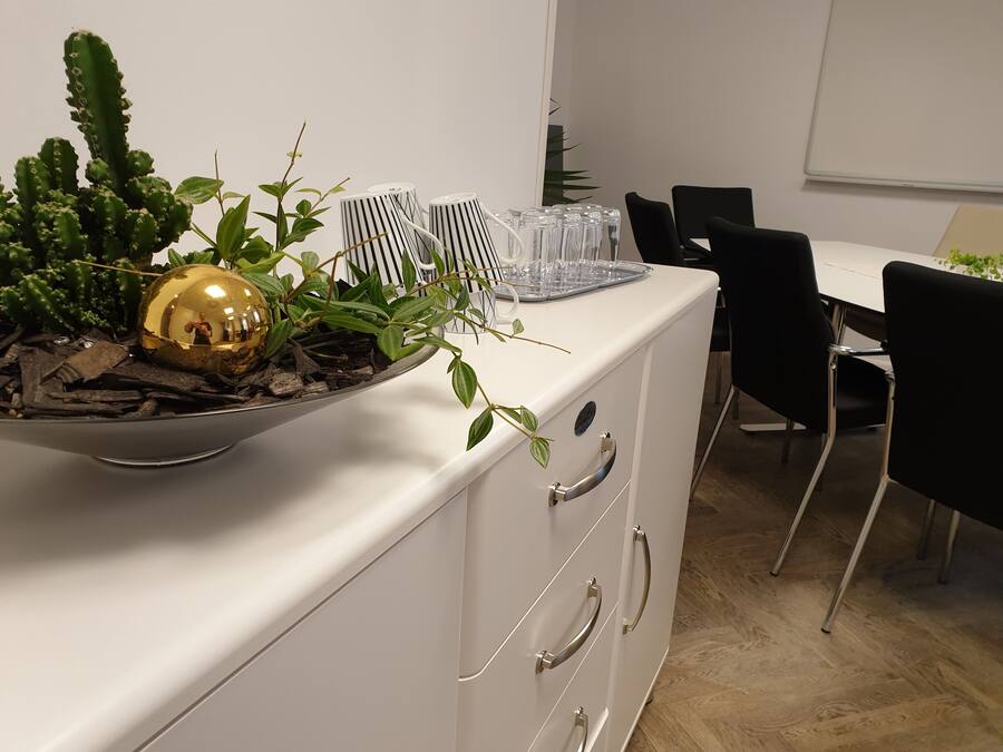 Et moderne kontormiljø med et hvidt skrivebord, sorte stole og en dekorativ plantekasse på et skab.