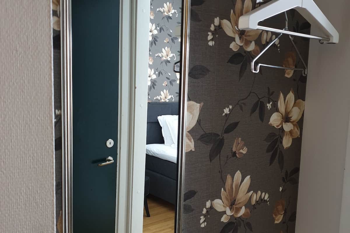 A room with a mirror, a door, a bed, and a floral wallpaper.