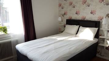 A neatly made bed with white bedding, a dark headboard, and a floral wallpaper pattern on the wall.